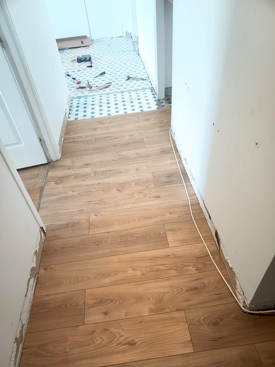 La sous-couche n'est déroulée qu'une pièce à l'avance : posée trop tôt, on la piétine et elle se déplace. Le couloir est verrouillé, la pièce suivante attend son tour.